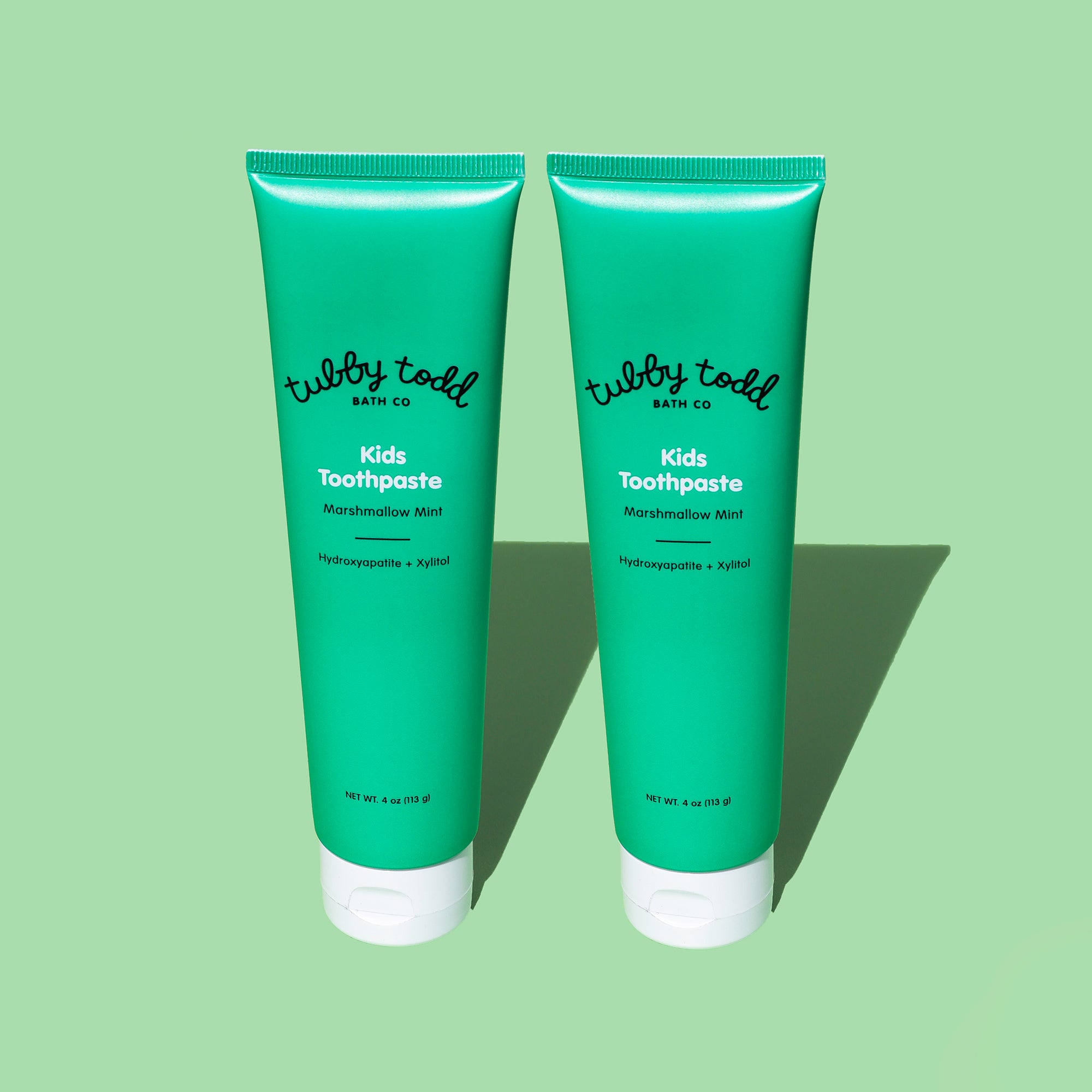 Two green tubes of Marshmallow Mint kids toothpaste on a light green background